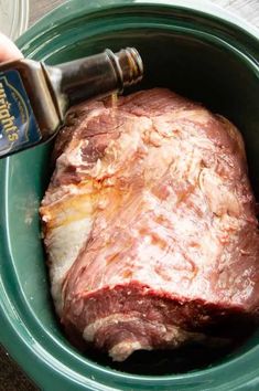 a person is pouring seasoning into a piece of meat in a green bowl