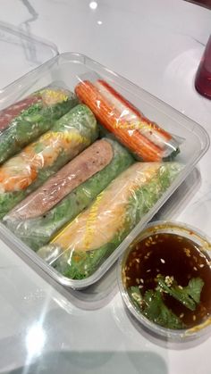 a plastic container filled with different types of vegetables and meats next to dipping sauce