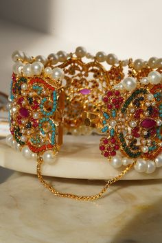 Adorn your wrist with the "Shama - Bangle," a luscious ensemble meticulously beautified by experts to infuse vibrant color into your festive attire. This exquisite bangle is embellished with the timeless beauty of multi-color stones, enhanced by a delicate addition of pearl moti, making it the perfect accessory to showcase elegance with contemporary style.The "Shama" bangle is designed with convenience in mind, featuring an openable design in the middle for easy wearing. It is a one-size-fits-mo Multicolor Intricate Design Gold-plated Jewelry, Gold Multi-stone Fusion Jewelry, Gold Fusion Multi-stone Jewelry, Multicolor Gold Plated Jewelry For Festivals, Jeweled Bangle Jewelry For Party, Festive Gold Multi-stone Jewelry, Multicolor Beaded Bangle Bracelets For Wedding, Multicolor Gold Plated Jewelry For Celebrations, Festive Gemstone Bracelet Jewelry