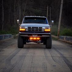 the truck is driving down the road with its lights on and there are trees in the background