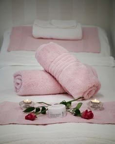 towels and candles on a bed with pink roses in the foreground, one rolled up to look like a rose