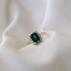 an emerald colored stone surrounded by diamonds on a white cloth with a ring in the middle