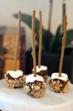 four desserts are arranged on a cake plate with sticks sticking out of them and topped with marshmallows