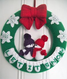 a knitted christmas wreath with two snowmen and a red bow hanging on the front door