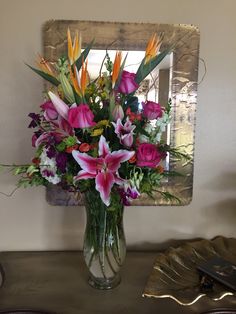 a vase filled with lots of flowers sitting on top of a table next to a mirror