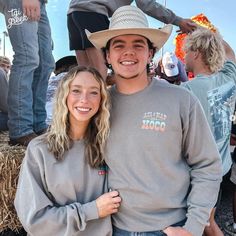 a man and woman standing next to each other in front of some hay bales