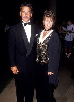 a man and woman standing next to each other wearing tuxedo's at an event