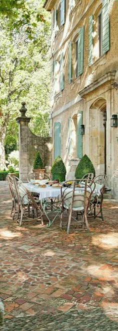 an outdoor dining table and chairs in front of a stone building with green shutters