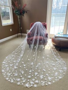 a wedding veil with flowers on it sits in the middle of a room next to a chair