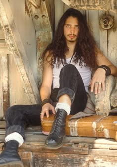 a man with long hair sitting on top of a wooden bench next to suitcases