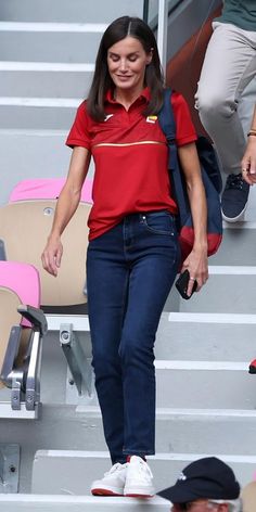 a woman walking up some steps wearing a red shirt and blue jeans