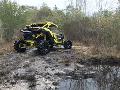 a yellow and black can - am spyder parked in the mud near some trees