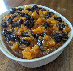 a bowl filled with fruit and raisins on top of a wooden table next to a cup of coffee