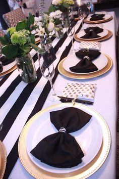 the table is set with black and white plates, napkins, silverware, and flowers