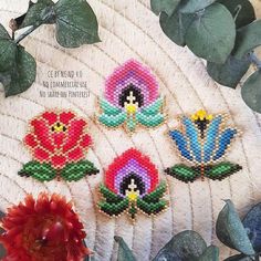 four cross stitch flowers sitting on top of a white plate next to some green leaves