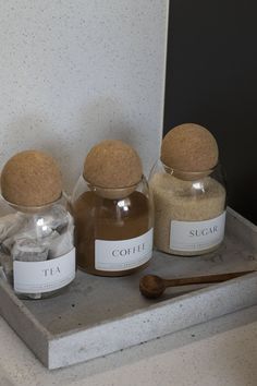 three jars filled with spices sitting on top of a counter next to a wooden spoon