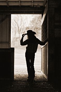 black and white photograph of a man in cowboy hat walking into an open barn door