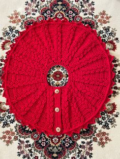 a red crocheted blanket sitting on top of a rug