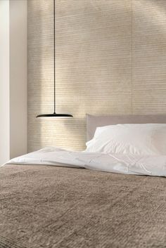 a bed with white sheets and pillows in a bedroom next to a wall mounted lamp