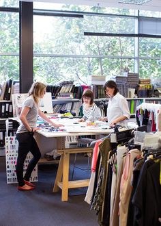 two women working at a table in an open room with lots of clothes on display