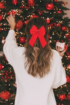 a woman in front of a christmas tree with a red bow on her head holding a cup