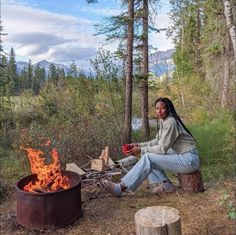 a woman sitting next to a fire in the woods