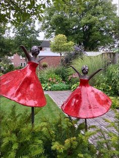 two red statues in the middle of a garden with trees and plants around them, one is wearing a red dress