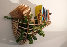 a wooden shelf with books and plants in it on the side of a white wall