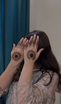 a woman holding her hands up to her face with hendi tattoos on it's palms