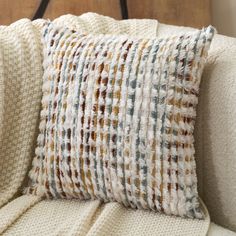 a close up of a pillow on a couch with a white blanket and wooden headboard in the background