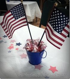 two american flags sticking out of a blue bucket filled with candies on a table