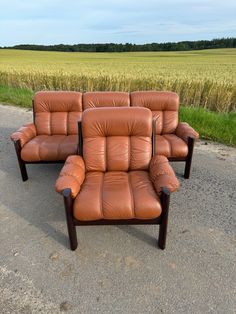 three leather couches sitting on the side of a road in front of a wheat field