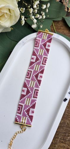 a pink and white beaded bracelet sitting on top of a tray next to flowers