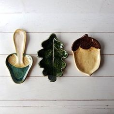 three ceramic leaf and acorn dishes on a white wooden surface, one is green and the other is brown