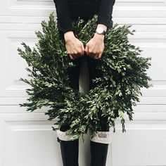 a woman standing in front of a white garage door holding a wreath with her hands