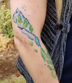 a woman's arm with a watercolor painting on it and mountains in the background