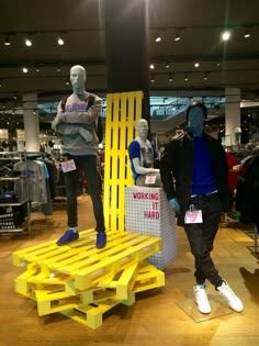 two mannequins are standing next to a yellow bench in a clothing store