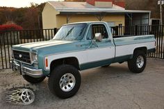 a blue and white pickup truck parked in front of a fenced off area with a dog laying on the ground