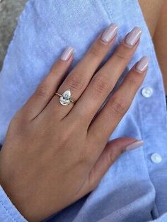 a woman's hand with a diamond ring on her left hand, wearing a blue shirt