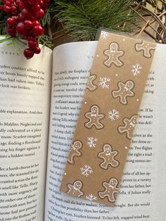 an open book with gingerbreads on it next to a christmas tree and berries