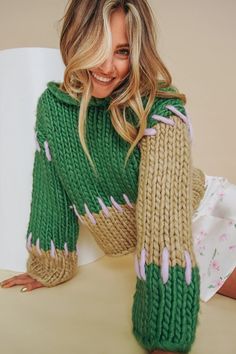 a woman in a green sweater is smiling and leaning on the table with her legs crossed