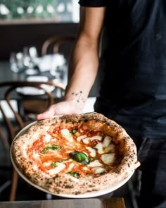 a man holding a pizza on top of a pan in front of a wooden table