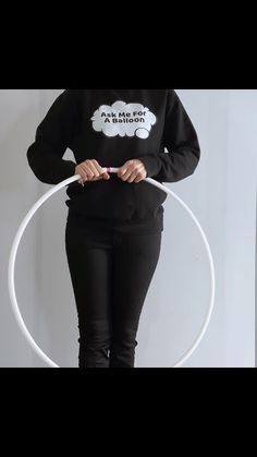 a woman holding a hoop while standing in front of a white wall and wearing a black sweatshirt