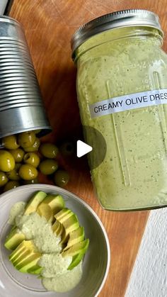 a bowl of green olives next to a jar of creamy olive dressing