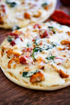 two pizzas sitting on top of a wooden table covered in cheese and toppings