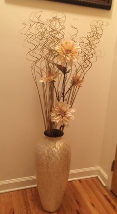 a vase filled with flowers on top of a hard wood floor next to a wall