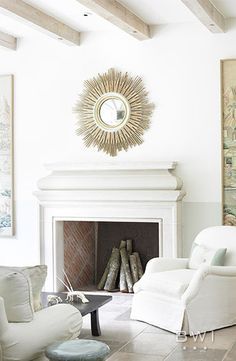 a living room filled with white furniture and paintings on the wall above it's fireplace