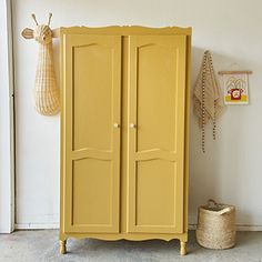 a yellow armoire sitting next to a basket on the floor in front of a white wall