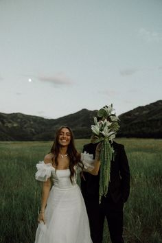 a bride and groom standing in a field with mountains in the backgroung