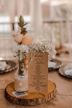 a table setting with flowers in a vase and menu on a wooden slice for seating